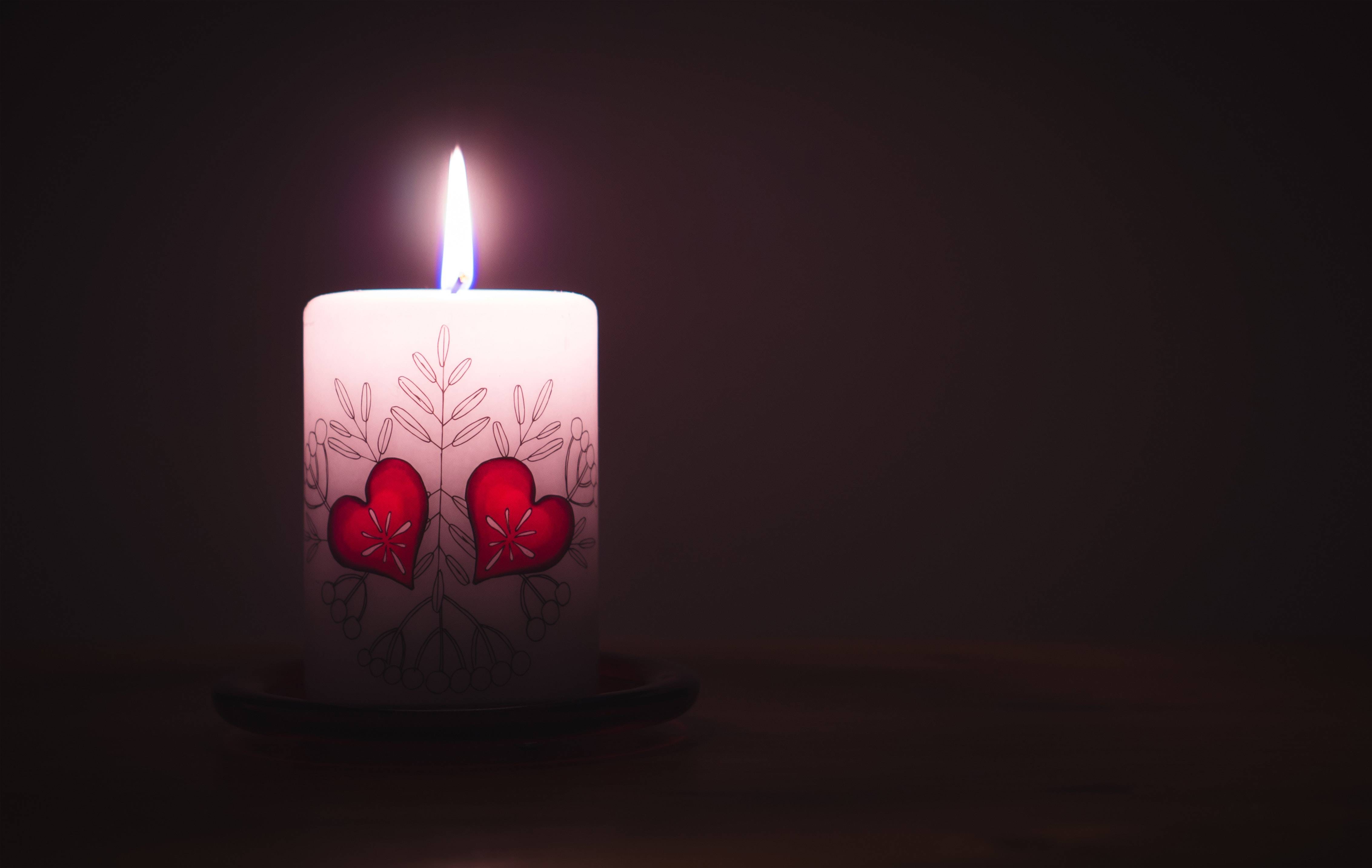 Single candle with two red hearts on it, against black backdrop