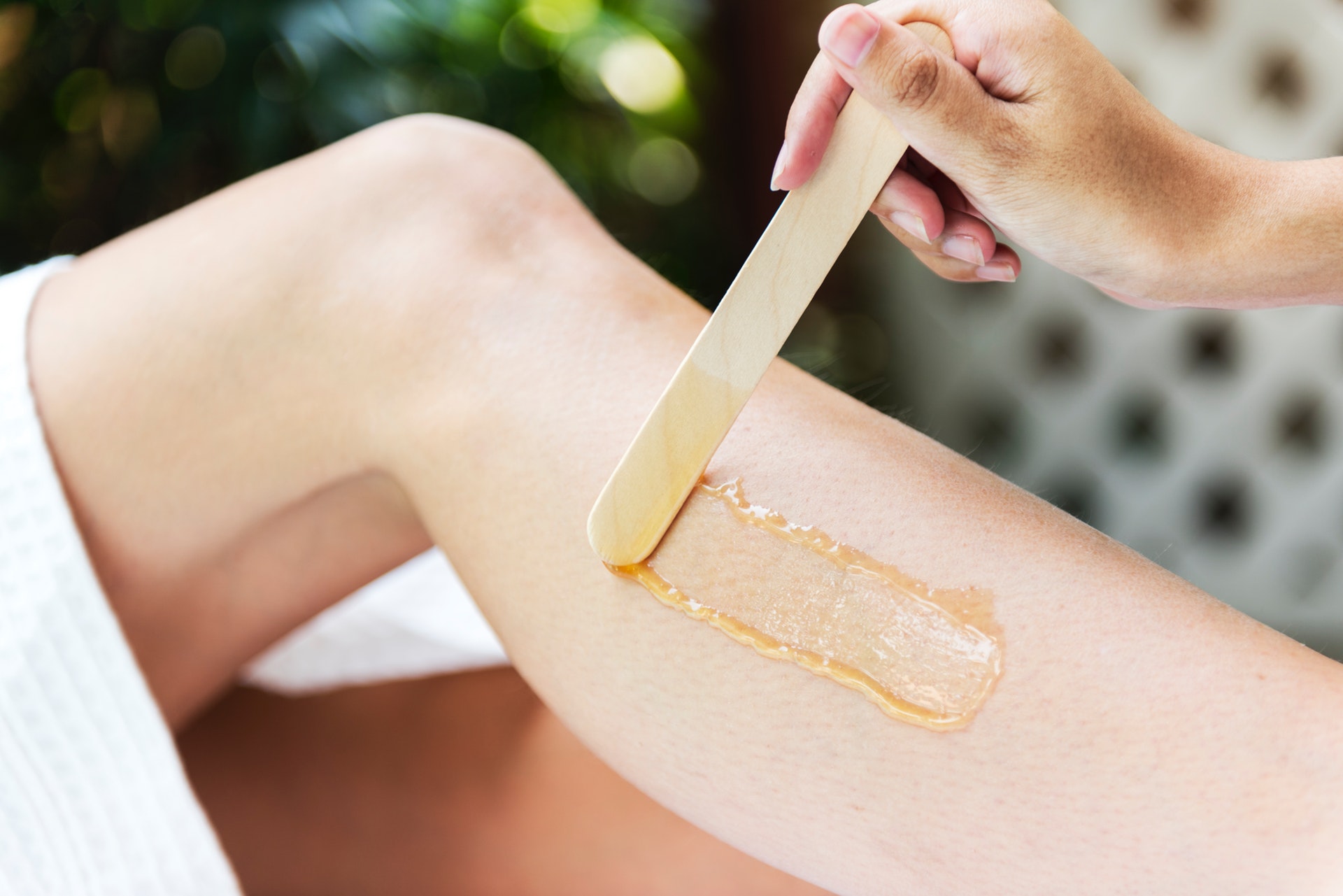 Hot wax being applied to woman's leg with wooden stick