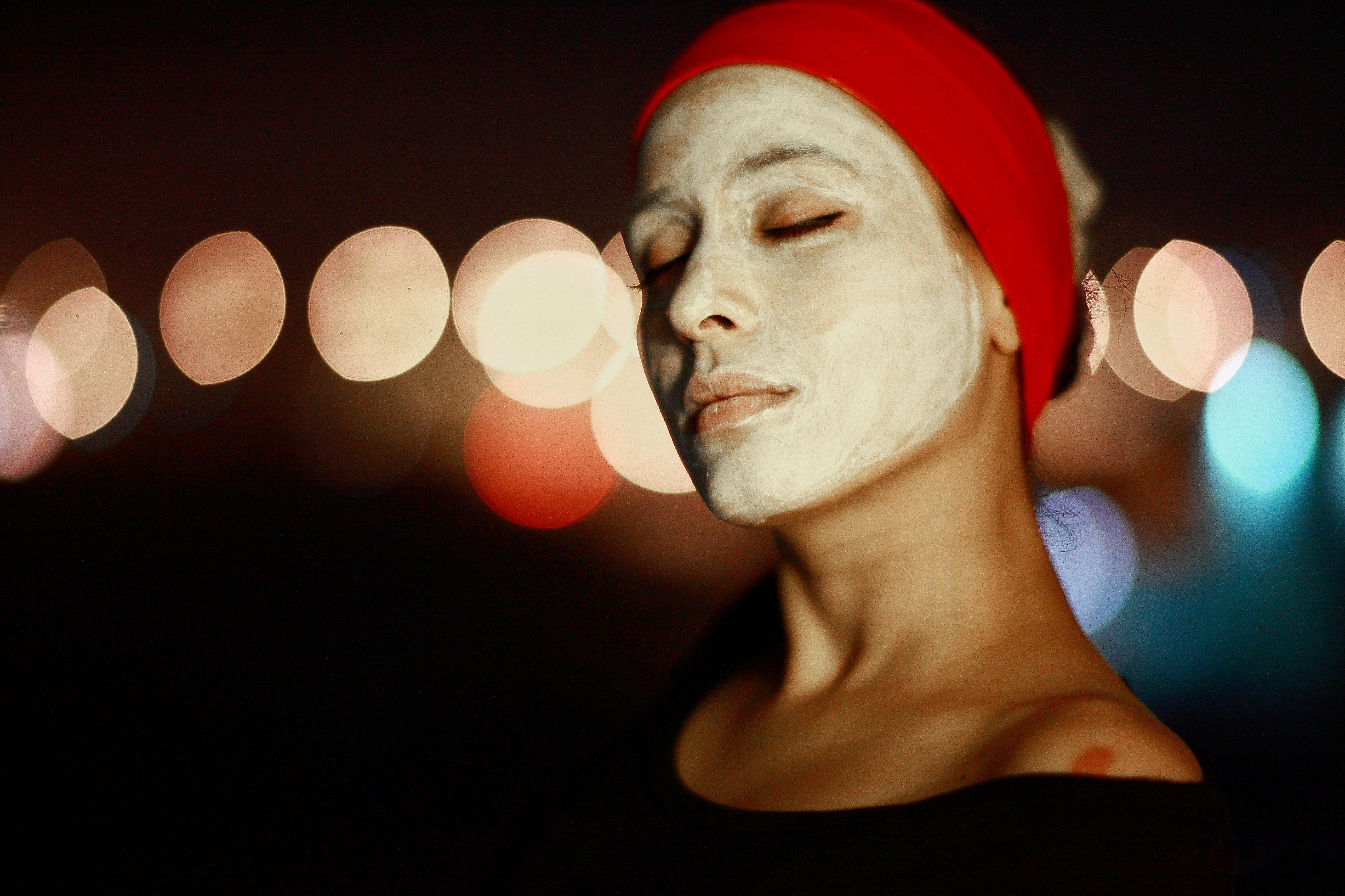 Woman with eyes closed and red headband, enjoying a facial mask