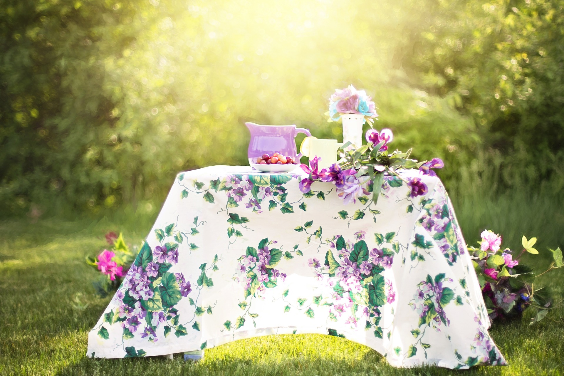 Table in a garden set up with purple flowers, a purple pitcher, and grapes