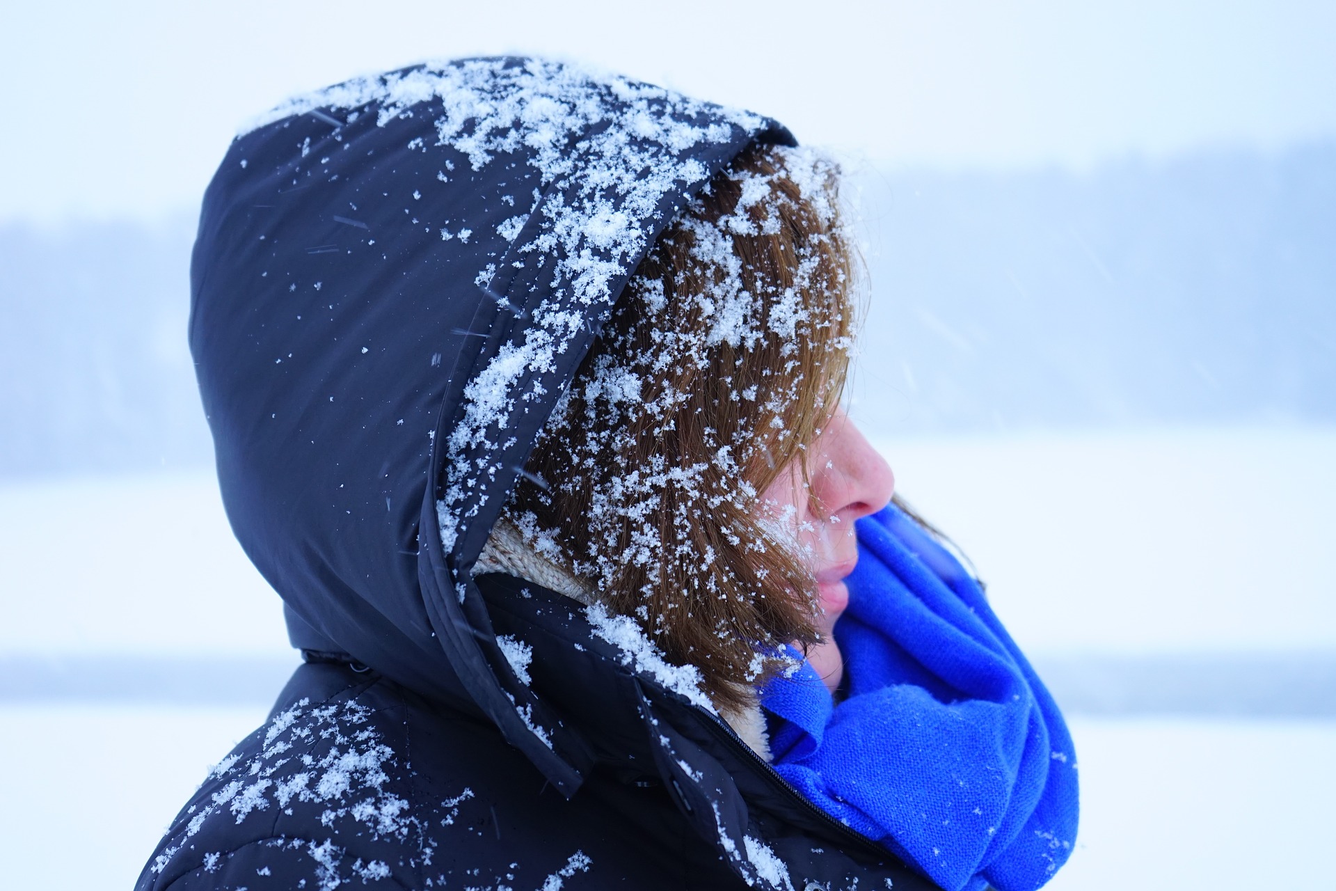 a side shot of a woman wearing a blue winter coat dusted with snow