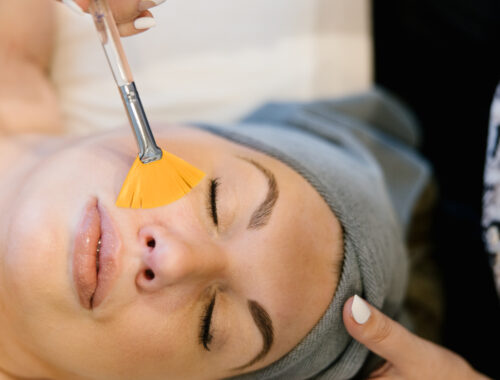 A woman relaxing with her eyes closed while receiving a Better Than Botox anti-aging facial at a luxury spa. A skincare specialist gently applies a treatment to her face, promoting a youthful, radiant glow. The setting is serene and calming, enhancing the experience of non-invasive skin rejuvenation.