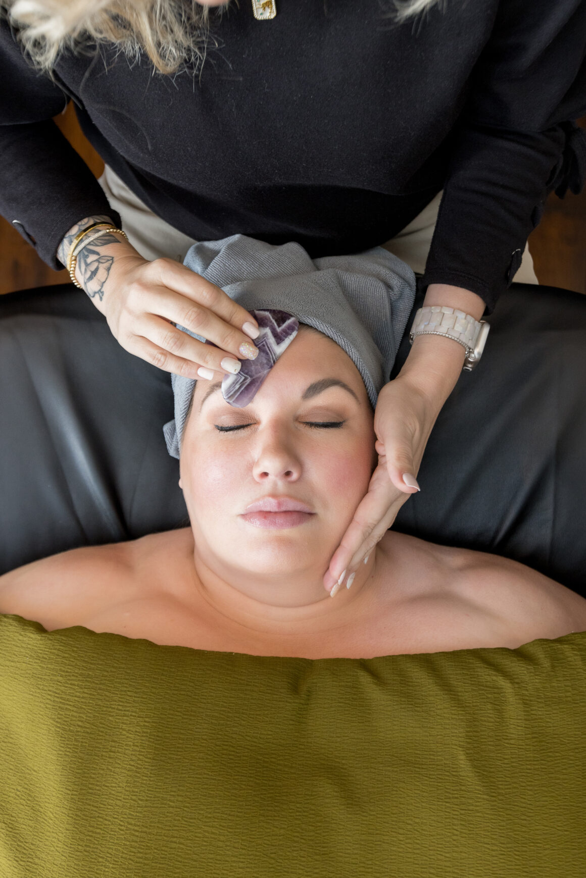 A woman relaxing with her eyes closed while receiving a gua sha stone facial massage at a Urban Oasis Nashville Day Spa. A skilled esthetician gently glides a jade gua sha tool across her face, sculpting, lifting, and promoting circulation for a firmer, more youthful complexion.