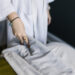 Woman in a spa robe gently pulls back soft white sheets, preparing to receive a peaceful spa treatment.