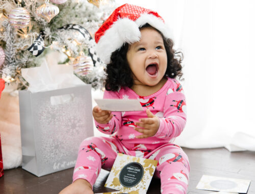 Excited baby laughing with spa gift cards from Urban Oasis Nashville, promoting the holiday Black Friday and Small Business Saturday spa sale.